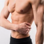 A close-up side-angle view of a fit, shirtless man’s muscular torso and arm, highlighting the clean, contoured borders of his pectoral muscle and abdomen to illustrate clinical benchmarks for selecting the Best Gynecomastia Surgeon UK.